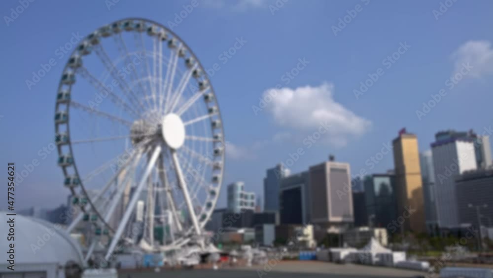 Blurred defocused view of big ferris wheel and amusement rides in central Hong Kong. Downtown skyline in the background Blurred defocused view of big ferris wheel and amusement rides in central Hong Kong. Downtown skyline in the background