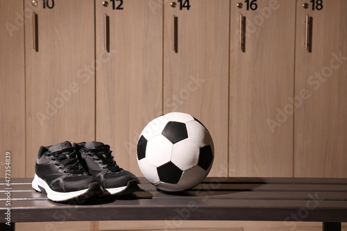 Soccer ball and sneakers on wooden bench in locker room photo