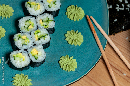 sushi rolls maki with cucumber and avacado on a blue curly plate on a wooden table 