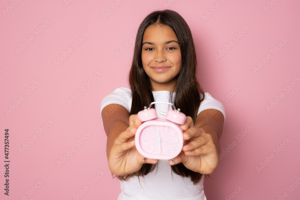 Beautiful smiling girl wearing casual white t-shirt showing alarm clock standing isolated over pink background. Beautiful smiling girl wearing casual white t-shirt showing alarm clock standing isolated over pink background.