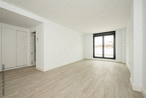 Large empty room with freshly painted walls with built-in wardrobe with sliding doors and large window leading to the terrace