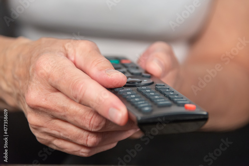 An older woman (old lady) holds the TV remote control in her hands. An elderly lady and her hands.