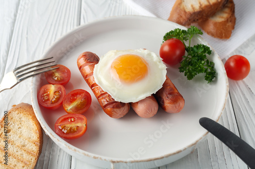 Scrambled eggs with sausages, tomatoes and toasts on a white wooden background