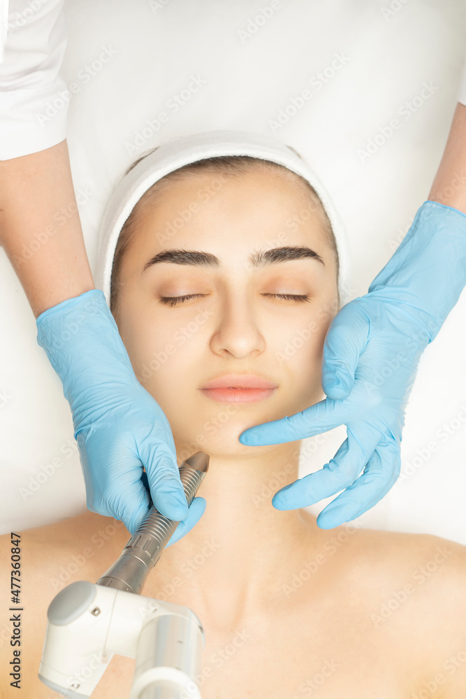Close-up face of a beautiful young woman receives a laser medicine procedure for facial skin rejuvenation. Fotona laser apparatus. Top wiev.vertical