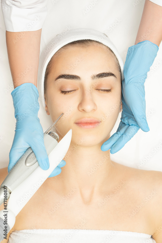 Close-up face of a beautiful young woman receives a laser medicine procedure for facial skin rejuvenation. Fotona laser apparatus. Top wiev.vertical Close-up face of a beautiful young woman receives a laser medicine procedure for facial skin rejuvenation. Fotona laser apparatus. Top wiev.vertical