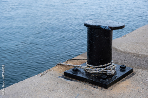 Ship mooring rope around a port bollard on harbor pier, rippled sea water background, copy space.