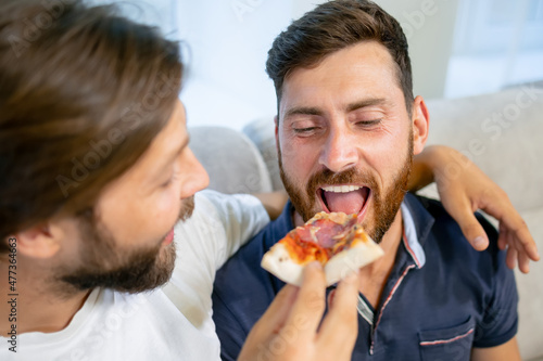 Handsome man gay family sitting on sofa  eating pizza together. Attractive romantic male lgbtq couple celebrate anniversary  spend time have dinner in kitchen in house. Homosexual-LGBTQ concept