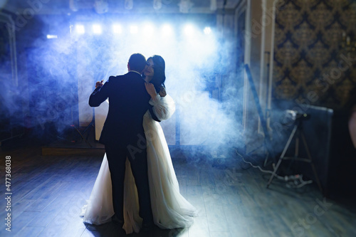 Canvas the bride and groom in wedding dresses dance in a dark hall in heavy smoke