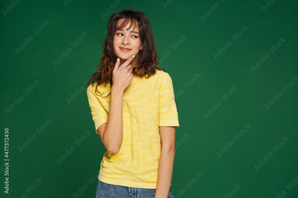 Smiling young pensive girl touching chin, looking aside on empty blank copy space for product, service advertising Smiling young pensive girl touching chin, looking aside on empty blank copy space for product, service advertising
