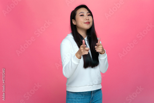 Confident young asian girl pointing to you at camera with fingers, choosing lucky one on pink studio background