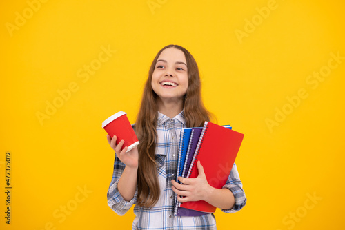 happy teen girl in checkered shirt holding coffee cup and notebook on yellow background, education