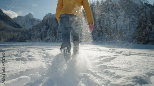 Medium shot - Woman running with a Border Collie dog in a snowy landscape, with snow flying around them, on a sunny day.