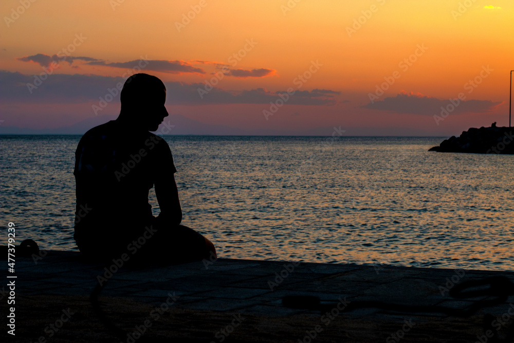 Teen boy in silhouette looking at the distance at sunset