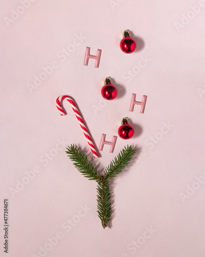Hohoho Christmas cocktail. Candy cane, red bauble and Xmas tree branch on pastel light pink background. Minimalistic winter holidays greeting card. Creative New Year flat lay concept.