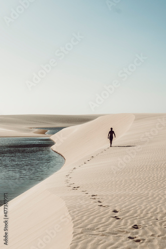 Lençóis Maranhenses - Lonely guy walking away leaving footsteps on the dunes of this brazilian national park photo