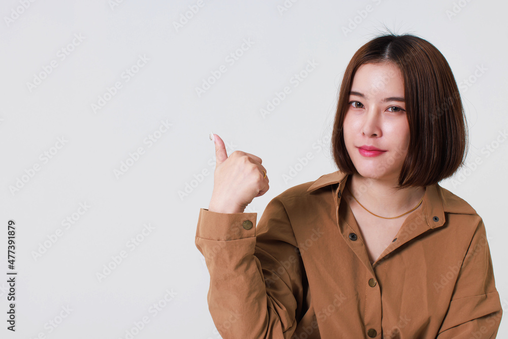 Studio cutout shot of Asian young pretty short hair female model in long brown coat jacket stand smile crossed arm hold thumb up pointing presenting product on blank copy space on white background Studio cutout shot of Asian young pretty short hair female model in long brown coat jacket stand smile crossed arm hold thumb up pointing presenting product on blank copy space on white background