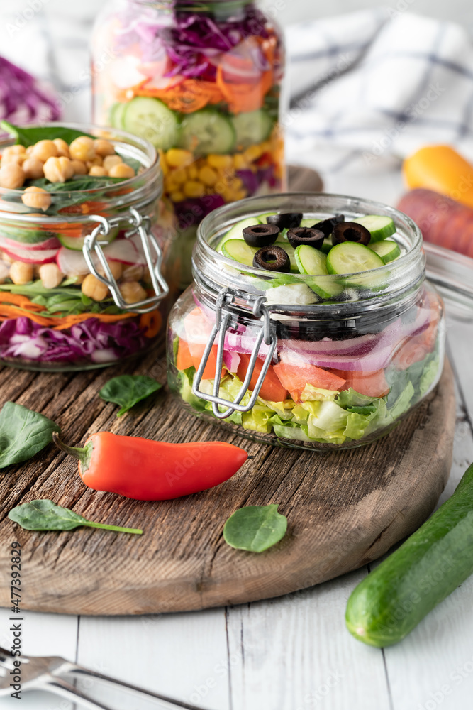 Jars filled with freshly made salad on a rustic wooden board.