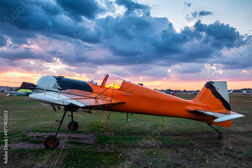 Orange sports airplane parked at the airfield at scenic sunset