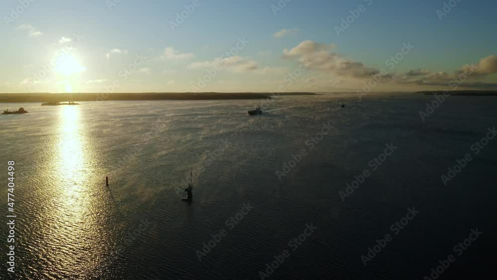 Aerial drone view of a general cargo vessel silhouette making way ahead during morning sunlight in finnish archipelago. Light sea fog forming on the rippled surface of the sea. Aerial drone view of a general cargo vessel silhouette making way ahead during morning sunlight in finnish archipelago. Light sea fog forming on the rippled surface of the sea.