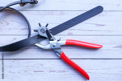 Metal hole puncher for belt holing with belt on white wood table -Device for punching holes in sewing industry