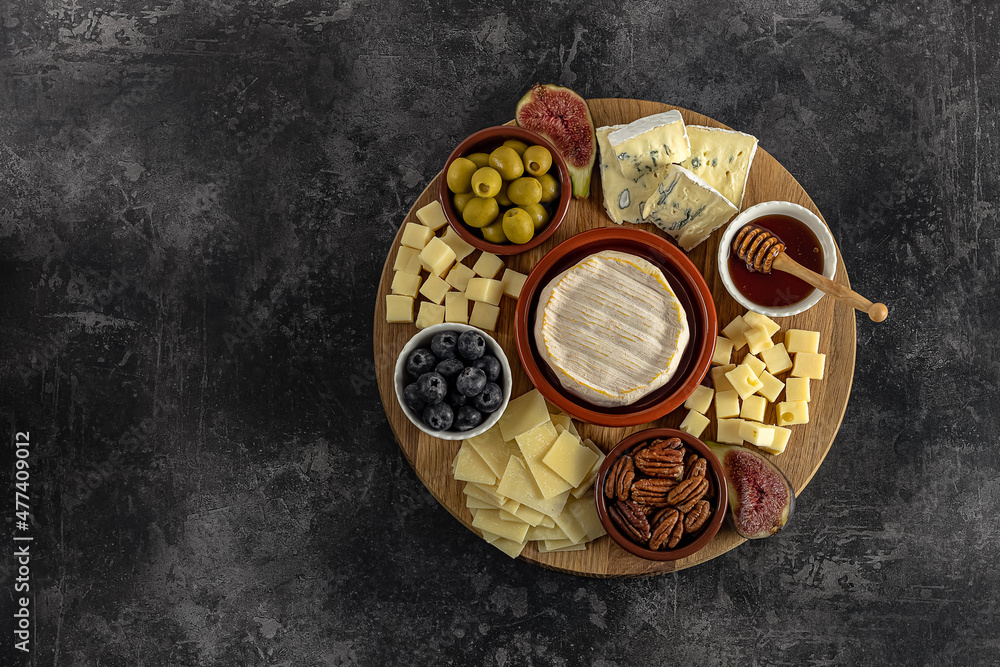 Top view of a tasty cheese plate with berries, honey, nuts, olives, and cheese varieties on a wooden board. Gourmet food, copy space.
