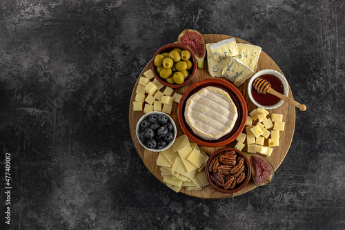 Top view of a tasty cheese plate with berries, honey, nuts, olives, and cheese varieties on a wooden board. Gourmet food, copy space. © Jane Vershinin