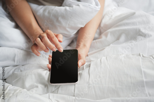 Woman's hand using blank screen smartphone on white bed. Clipping path.