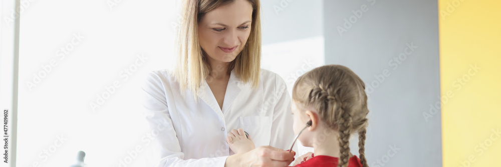 Doctor pediatrician putting stethoscope on little girl in clinic Doctor pediatrician putting stethoscope on little girl in clinic