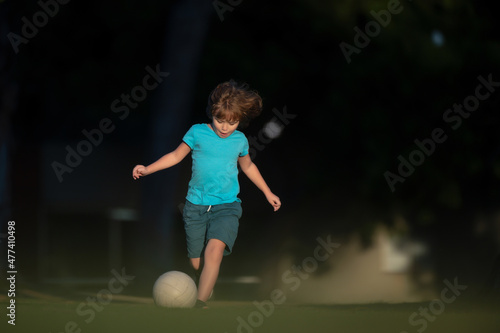 Kid playing soccer, happy child enjoying sports football game, kids activities, little soccer player. Child playing football on the playground in park. © Volodymyr