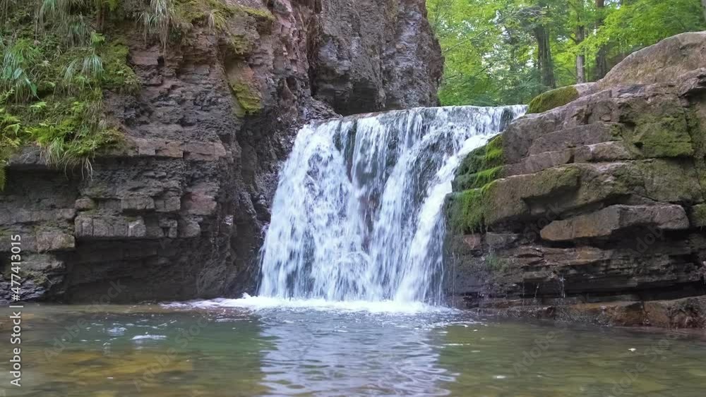 Waterfall on mountain river with white foamy water falling down from rocky formation in summer forest Waterfall on mountain river with white foamy water falling down from rocky formation in summer forest