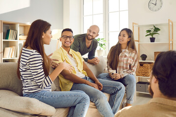 Diverse group of happy young friends having fun together. Smiling mixed race multi ethnic people talking and sharing interesting stories while sitting on the sofa at a friendly get-together at home