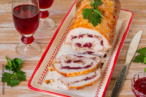 Cold appetizer or hot dish, pork roll with dried cranberries and walnuts on a clay dish on a light wooden background. Served with cranberry sauce.