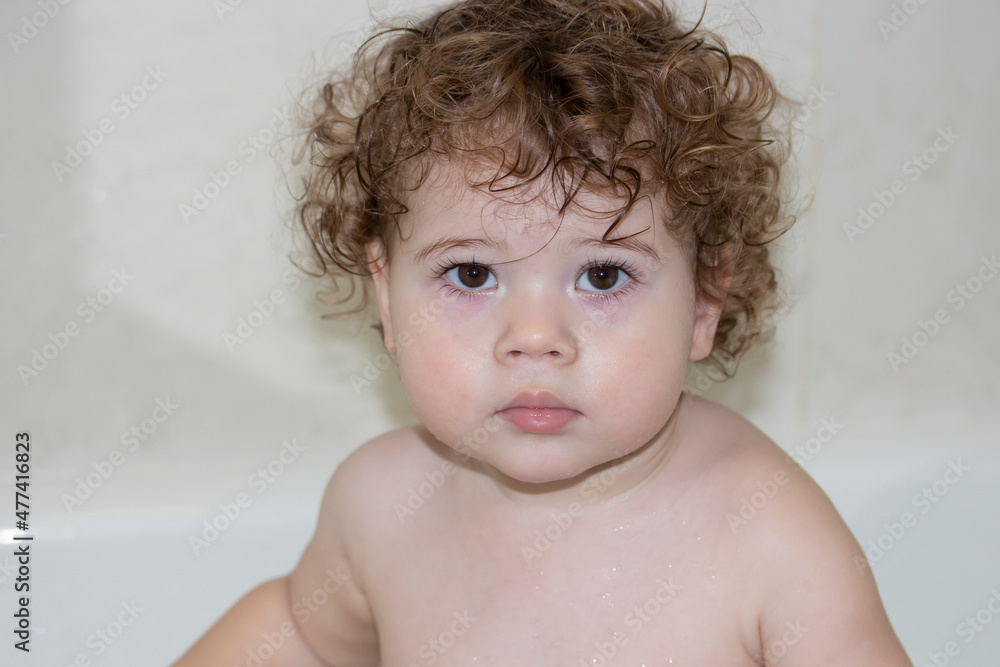 Little caucasian girl 1 year old takes a bath, wet face of a curly toddler Little caucasian girl 1 year old takes a bath, wet face of a curly toddler