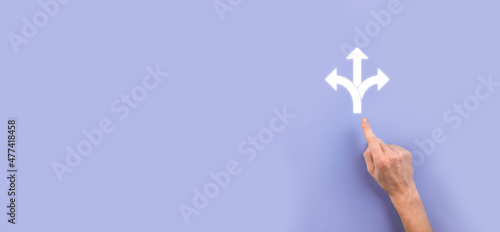 Fototapeta Naklejka Na Ścianę i Meble -  Male hand holding icon with three directions icon on dark background. Doubt, having to choose between three different choices indicated by arrows pointing in opposite direction concept. Ways