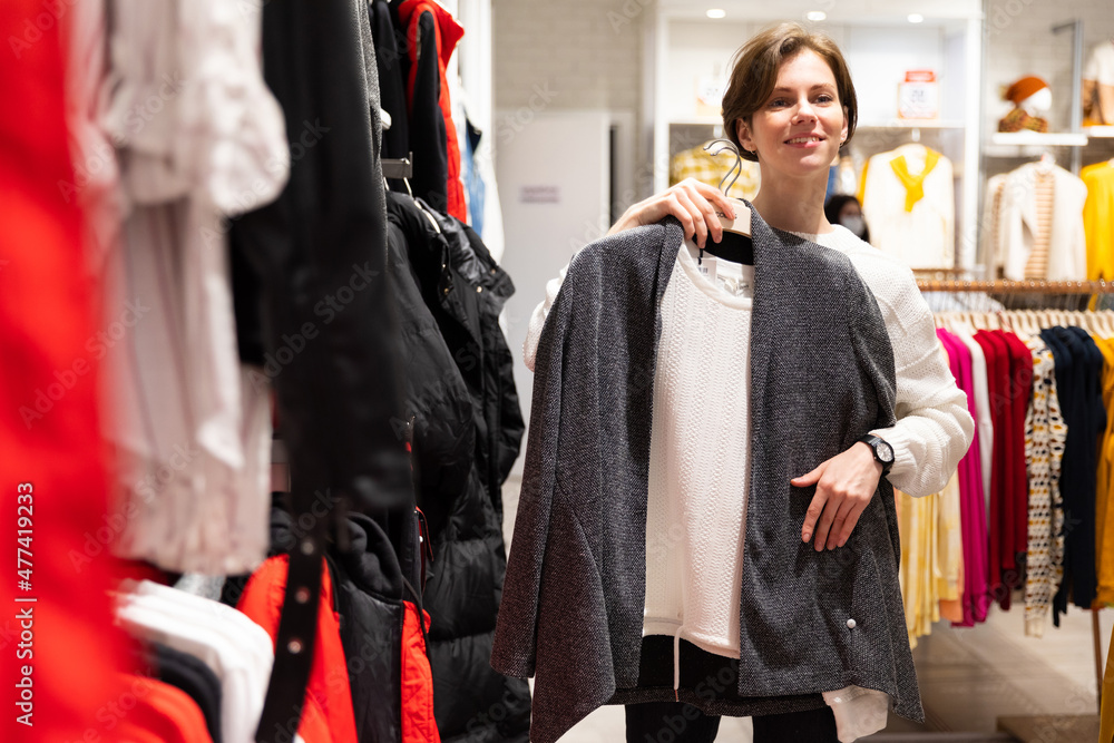 Photo of young attractive brunette woman with a short haircut in a white sweater chooses stylish and casual clothes in a store in a shopping mall. Shop concept Photo of young attractive brunette woman with a short haircut in a white sweater chooses stylish and casual clothes in a store in a shopping mall. Shop concept