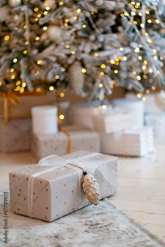 Gift box wrapped in wrapping paper with pine cone on background of new year lights bokeh christmas tree.Copy space. Soft selective focus.