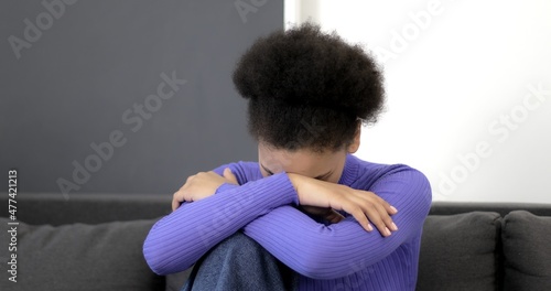 Sleepy black woman yawns while sitting on a sofa. Afro american woman in white t-shirt falls asleep.
