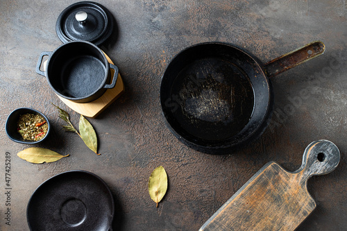 Empty kitchen utensils for cooking. Black Iron pot, fry pan,wooden cut biard and traditional herbs on dark background