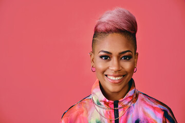 Portrait of a happy stylish young woman with pink hair and colofrful fashion jacket on pink background