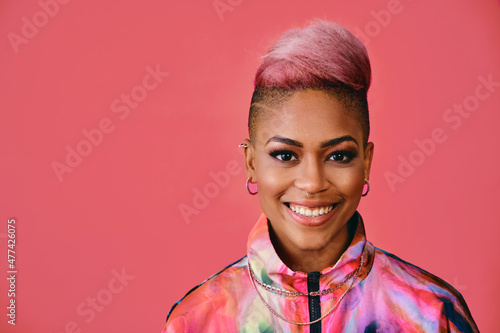 Portrait of a happy stylish young woman with pink hair and colofrful fashion jacket on pink background