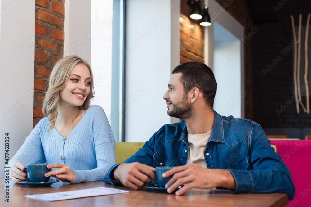 Fototapeta premium happy couple looking at each other while sitting near coffee cups