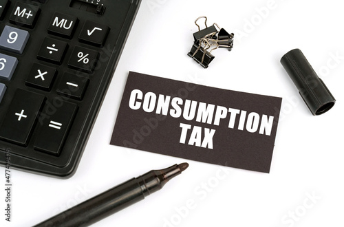 On a white table there is a calculator, a marker and a black plate with the inscription - Consumption Tax photo