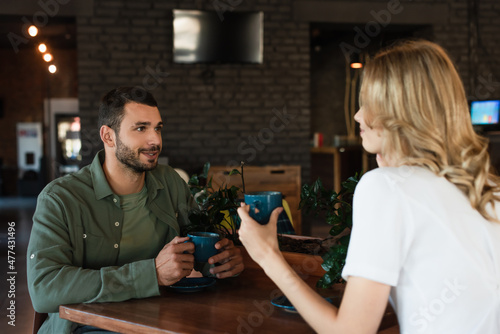 young man talking to blurred girlfriend during date in cafe