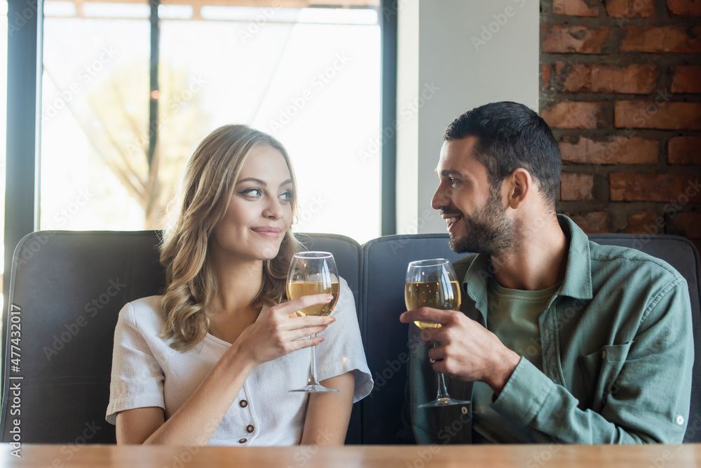 happy young couple with wine glasses looking at each other while spending time in cafe