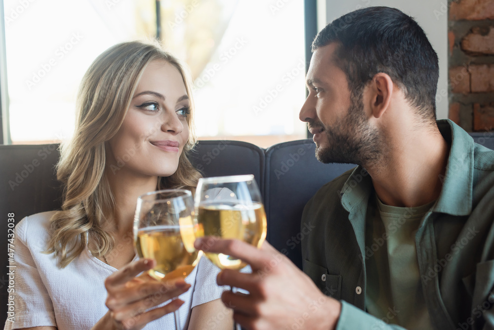 cheerful couple clinking wine glasses and looking at each other in restaurant