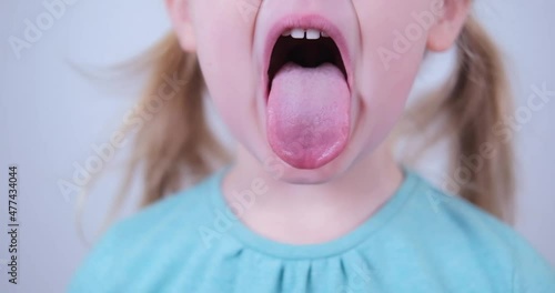 Little blond girl show tongue, throat. Kid training of muscles speech therapy. photo