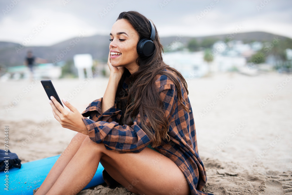 Hot female surfer relaxing on the sandy beach. Beautiful woman with headphones listening the music..