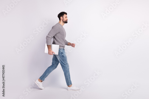 Full body profile side photo of young man walk hold laptop representative isolated over grey color background