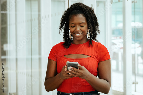 happy african american woman student in red top using smartphone