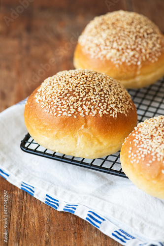 Freshly baked burger buns with sesame seeds on a wooden background.